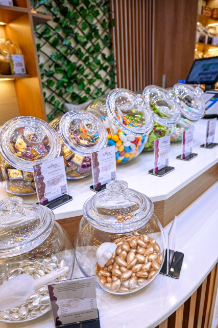 A white counter displays glass jars of colorful sweets, with illuminated shelves visible in the background.