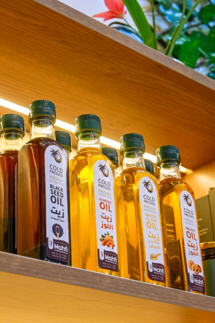 Bottles of cold pressed oils arranged in a row on a wooden shelf.