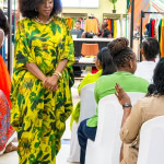 A guest in a green and yellow floral dress stands among the audience at Style, Shop & Sip