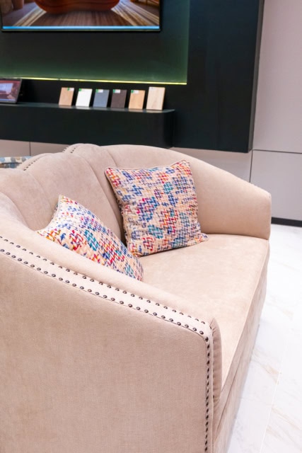 Beige upholstered sofa with two multicolored patterned cushions.