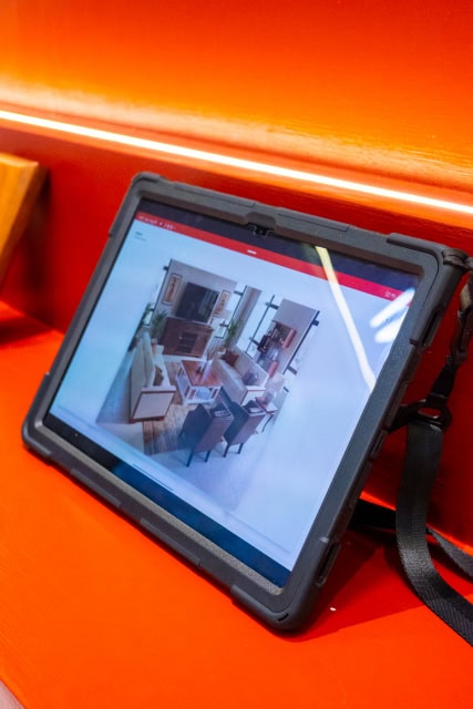 Tablet showing a furniture showroom image on a red display counter