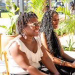 Smiling Attendees Seated Outdoors Two women smiling while seated outdoors beside palm plants.