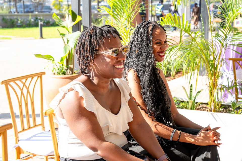 Smiling Attendees Seated Outdoors Two women smiling while seated outdoors beside palm plants.