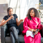 Speaker Leads a Wellness Discussion A speaker gestures while holding a microphone during a discussion with another woman seated beside her.