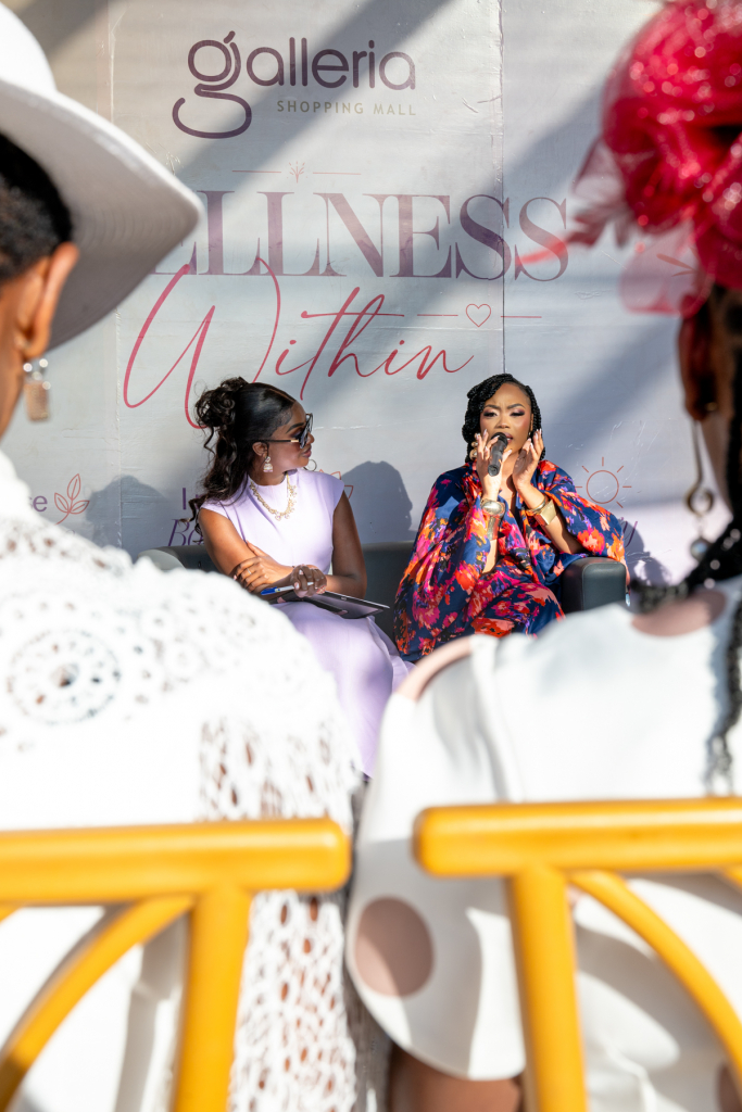 Woman speaking into a microphone beside another panelist in front of a Wellness Within backdrop