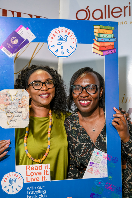 Two smiling women posing behind a blue travelling book club photo frame