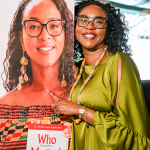 Author Portrait Display and Guest Smiling woman in green poses beside a large portrait display showing a woman holding the book Who Moved My Cheese?