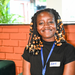 Smiling event staff member A smiling event staff member with beaded braids wears a blue lanyard and a name tag.