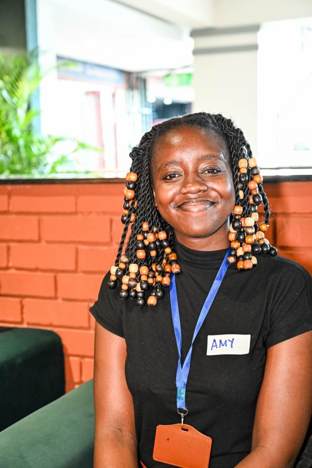 Smiling event staff member A smiling event staff member with beaded braids wears a blue lanyard and a name tag.