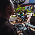 Outdoor Keyboard Performance Keyboard player performing outdoors with a microphone and laptop as people sit nearby.