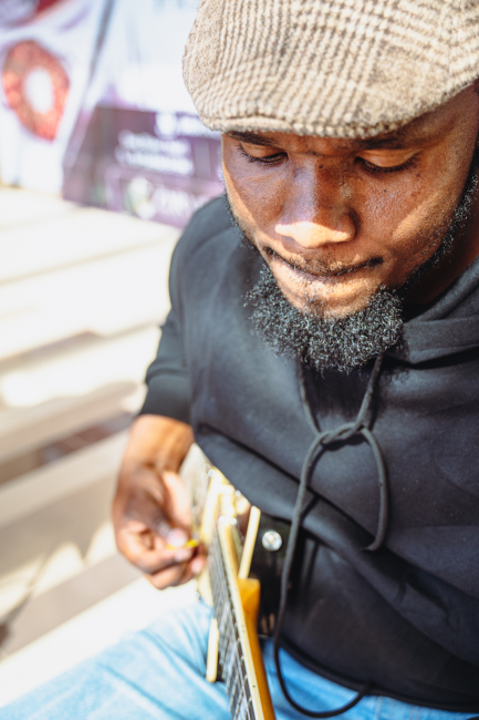 Musician in a knit cap looking down while holding a stringed instrument.