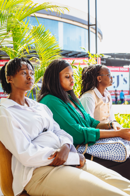 Three attendees sit together near palm plants outside the mall event area