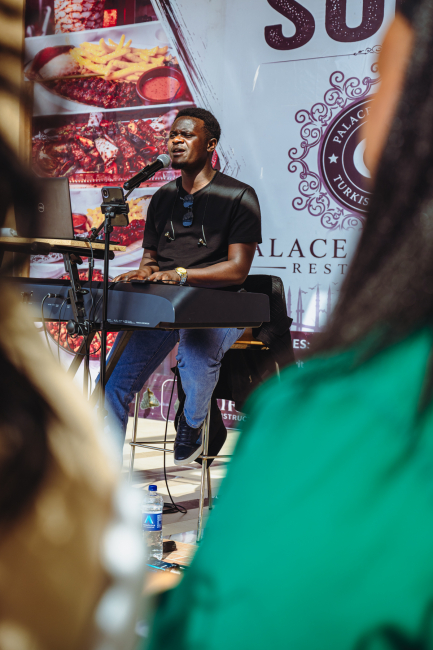 A keyboard player performs for an audience in front of a restaurant backdrop