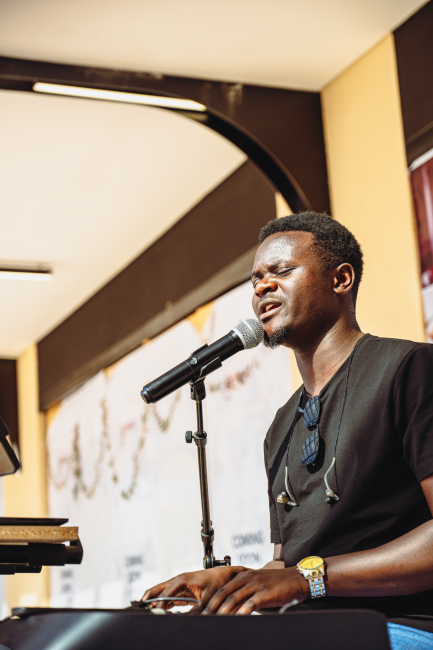 A musician sings into a microphone while playing a keyboard
