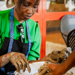 A participant in a bright green shirt works with an instructor at a pottery wheel