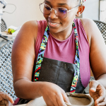 Smiling participant forming a small clay vessel at a table