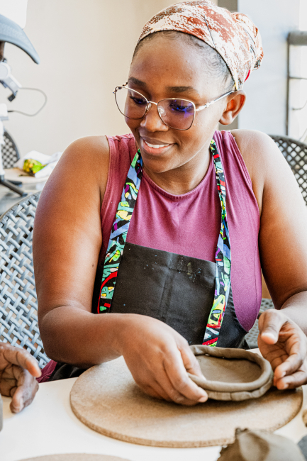 Smiling participant forming a small clay vessel at a table