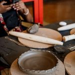 Unfinished shallow clay bowl surrounded by pottery tools on a workshop table.