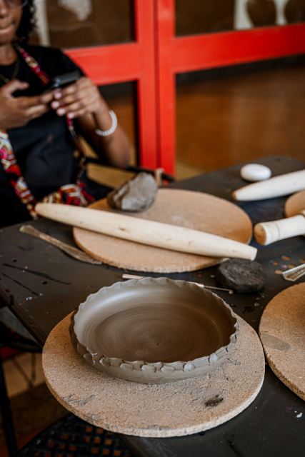 Unfinished shallow clay bowl surrounded by pottery tools on a workshop table.