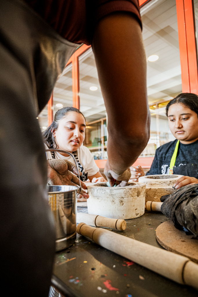 Participants work together with clay around a large container at a workshop table.