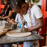 A young participant concentrates while shaping clay on a round work board.