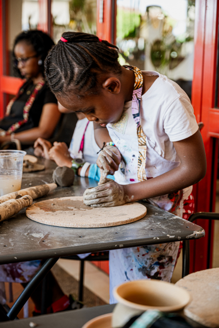 A young participant concentrates while shaping clay on a round work board.