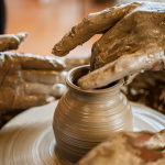 Clay-covered hands shaping a vessel on a spinning pottery wheel