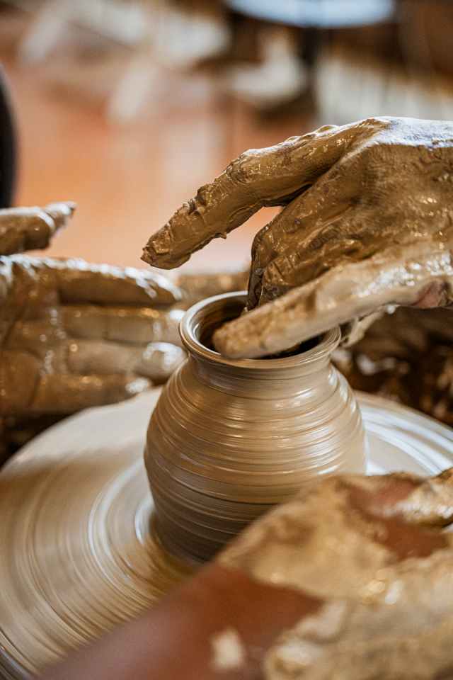 Clay-covered hands shaping a vessel on a spinning pottery wheel