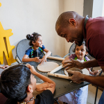 An adult instructor helps three children work with clay at a table.