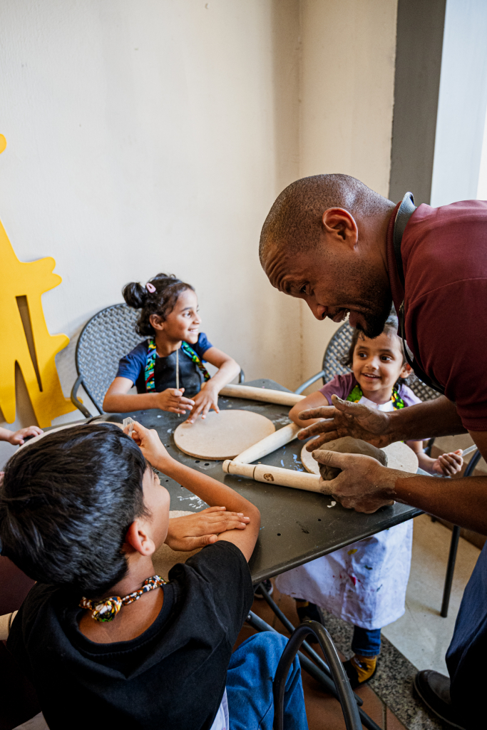 An adult instructor helps three children work with clay at a table.