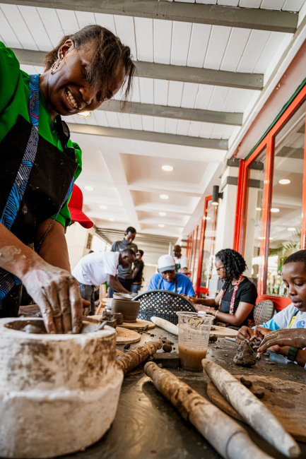 Smiling participant shapes clay at a pottery workshop while other people work in the background.