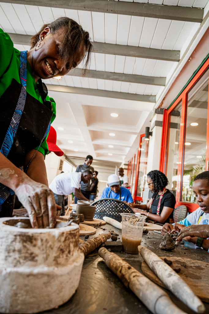 Smiling participant shapes clay at a pottery workshop while other people work in the background.