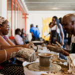 Participants work with clay around a pottery wheel holding a small unfinished vessel.