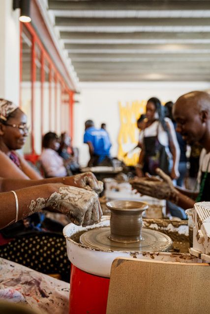 Participants work with clay around a pottery wheel holding a small unfinished vessel.