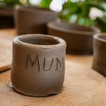 Handmade clay cup marked MUM on a pottery work surface.