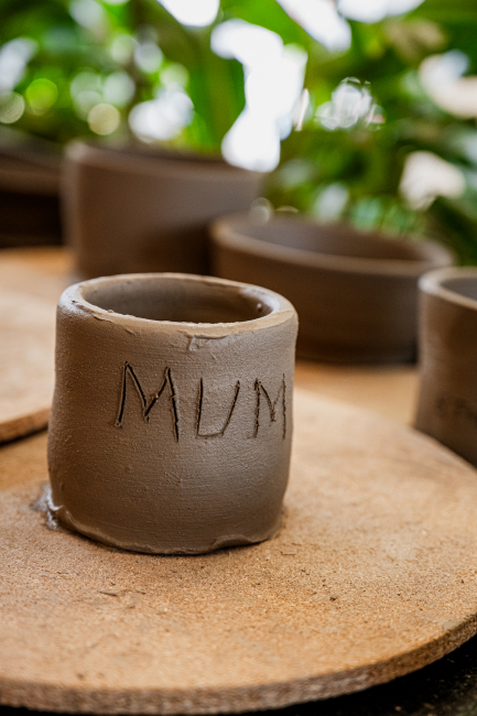 Handmade clay cup marked MUM on a pottery work surface.