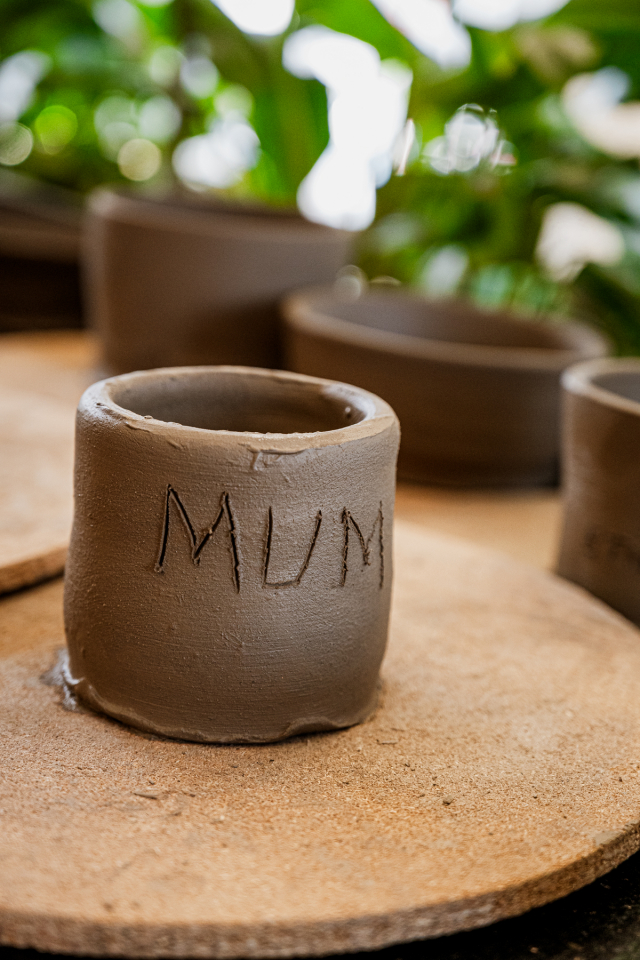 Handmade clay cup marked MUM on a pottery work surface.