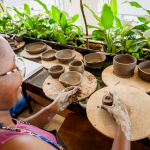 A participant shapes clay on a pottery wheel surrounded by handmade ceramic vessels.