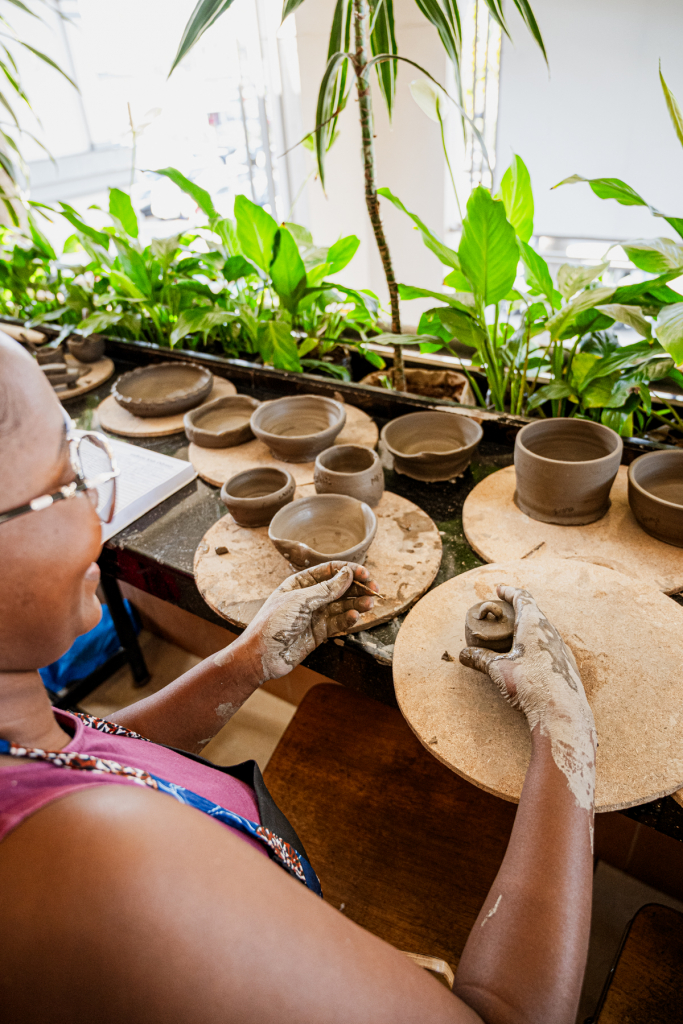 A participant shapes clay on a pottery wheel surrounded by handmade ceramic vessels.