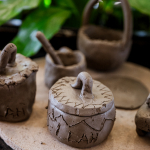 A small handmade clay pot with a looped handle sits among other clay vessels.