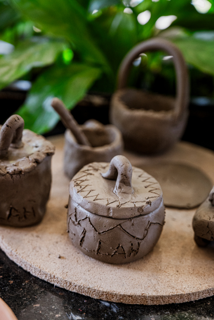 A small handmade clay pot with a looped handle sits among other clay vessels.