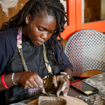 A participant concentrates while shaping a clay bowl at a workshop table.