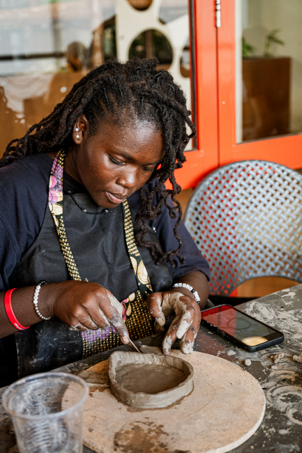 A participant concentrates while shaping a clay bowl at a workshop table.