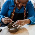 Smiling participant adds detail to a handmade clay bowl.