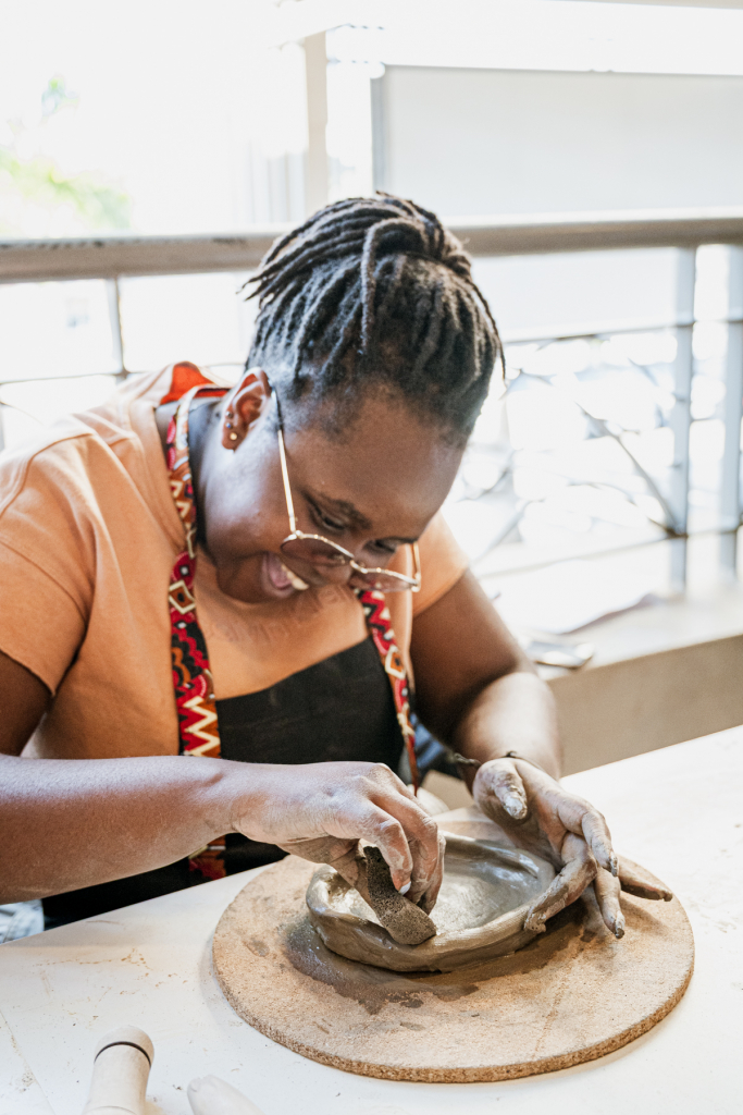 Woman in glasses and an apron shapes a clay dish by hand.