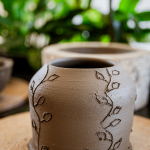 Brown ceramic vessel decorated with etched leafy vines.