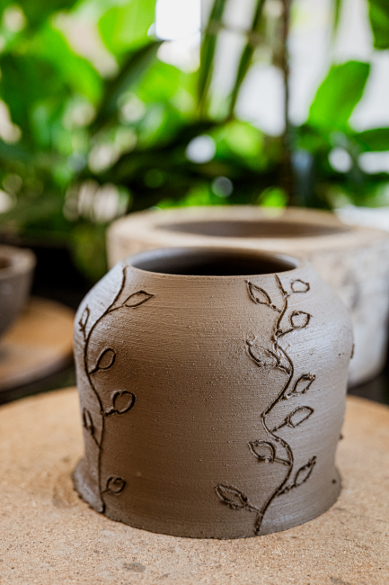 Brown ceramic vessel decorated with etched leafy vines.