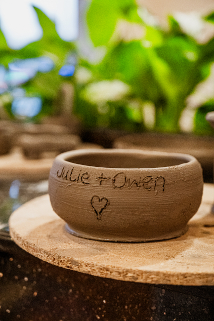 A handmade clay bowl with a handwritten message and heart engraving rests on a wooden board.