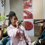 A singer in a pale pink shirt sings into a microphone during a live performance.