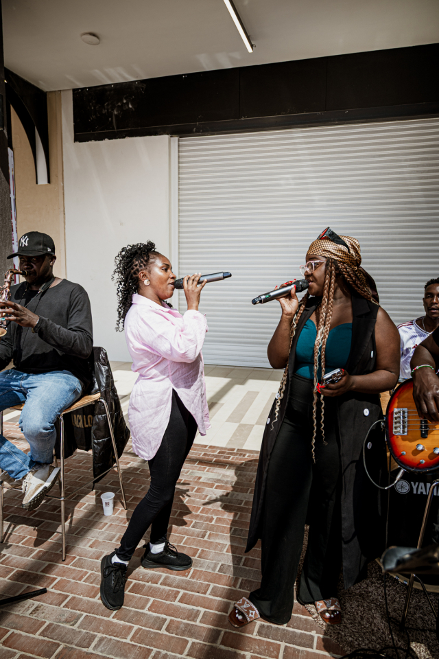 Two singers perform together with microphones while musicians accompany them.